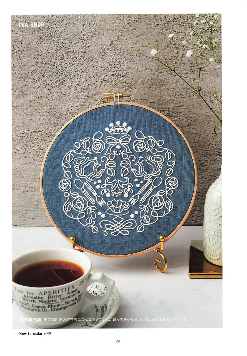 20221014_680 Tea shop embroidery pattern: a white rose-and-crown emblem with cutlery on blue linen in a hoop