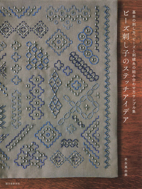 Cover of this Japanese beads sashiko embroidery book showing dense blue and silver geometric sashiko bead stitch patterns on grey linen fabric.
