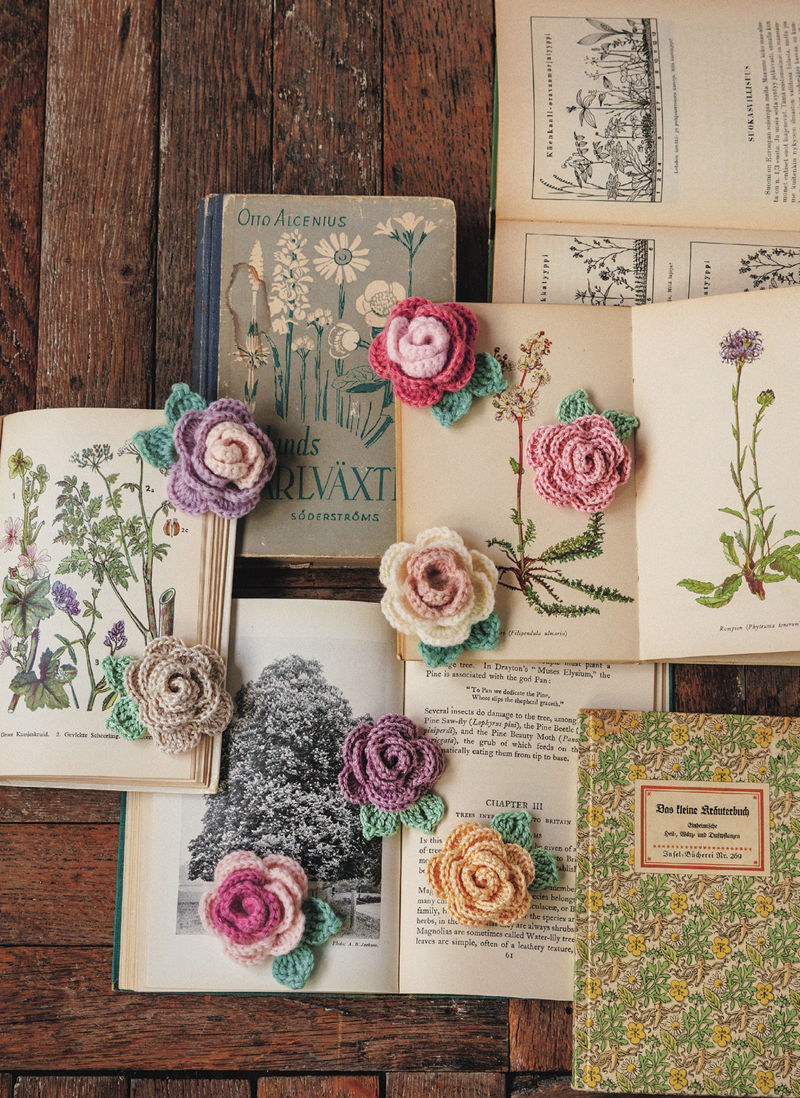 00006 Crochet rose motif brooches in pink, lilac and cream scattered across open vintage botanical booksCrochet rose motif brooches in pink, lilac and cream scattered across open vintage botanical books