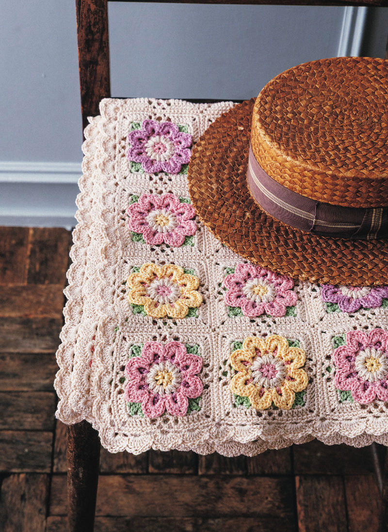 00017 Close view of a floral granny square pattern with scalloped cream edging, styled with a straw boater