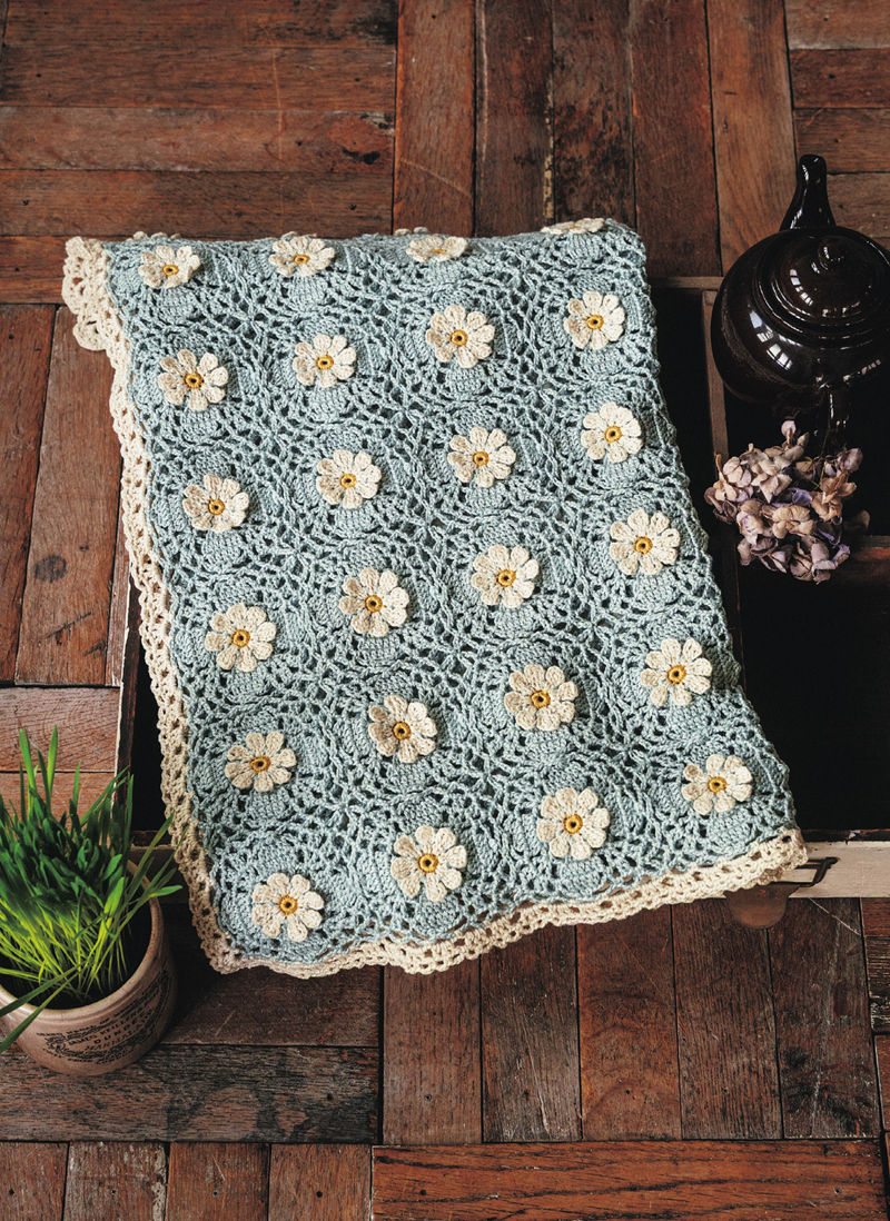 00029 Folded lightweight crochet lace blanket showing openwork mesh and scattered cream daisy flowers