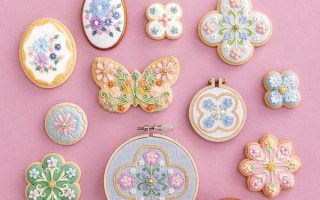 Pink flat-lay of icing-cookie designs worked in thread, beads and pearls — the cover of this cookie embroidery patterns book.