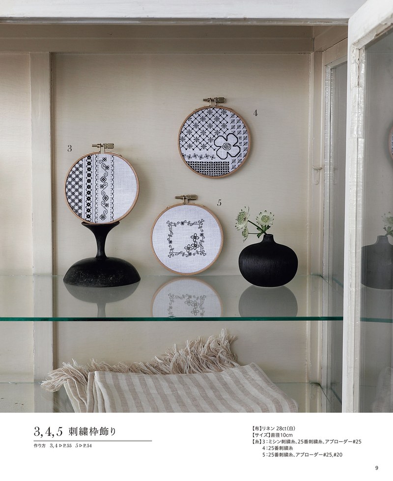 1489-00011 Embroidery hoops with black geometric stitching displayed on a glass shelf beside a vase