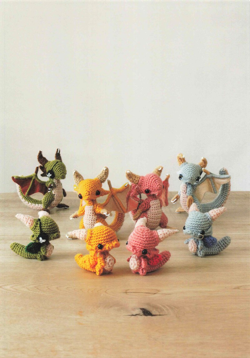 1495-04232026184535_007 Orange, green, pink and gray crochet dragons gathered on a wooden table, amigurumi monsters to make
