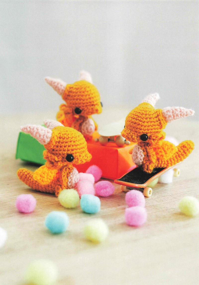 1495-04232026184535_014 Orange crochet dragons playing on a toy skateboard with colorful pom-poms