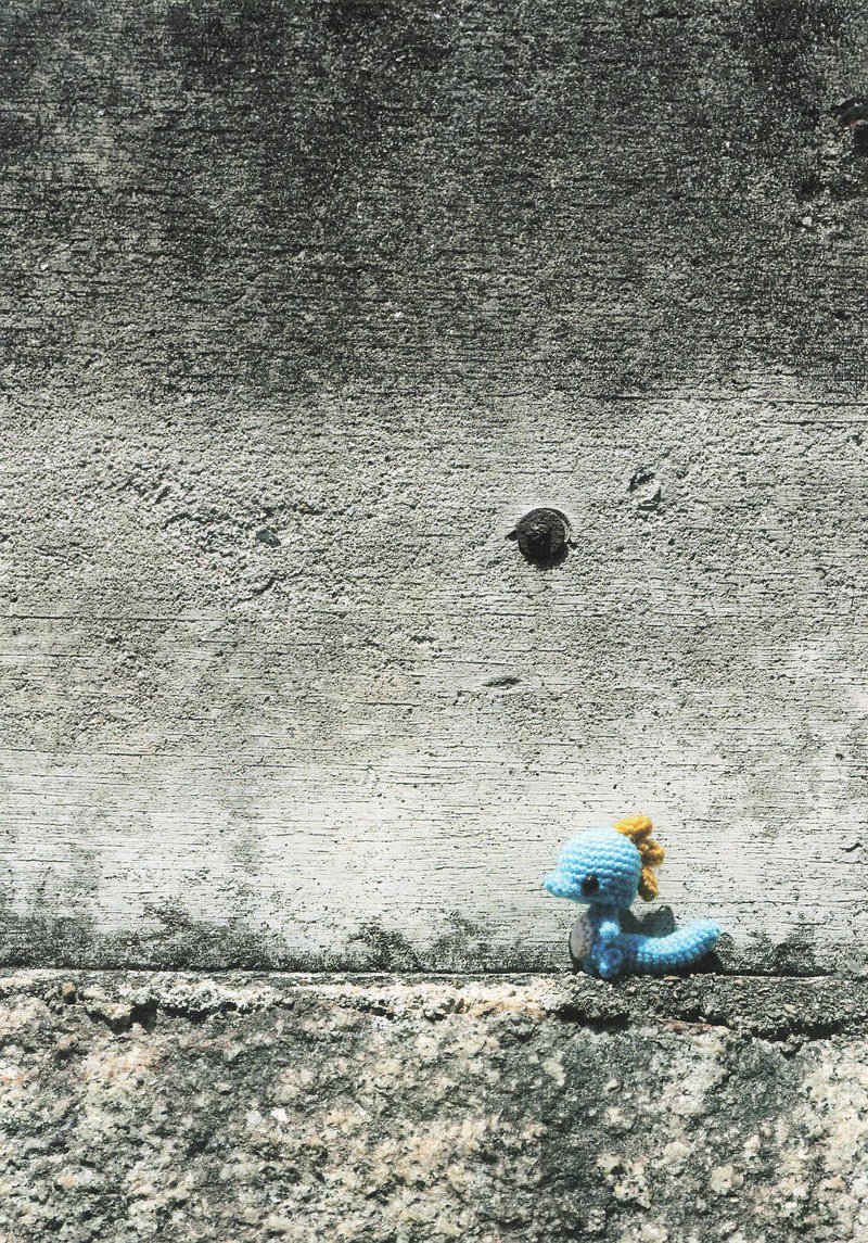 1495-04232026184535_025 A single tiny blue crochet dragon on a concrete wall, a small amigurumi creature up close